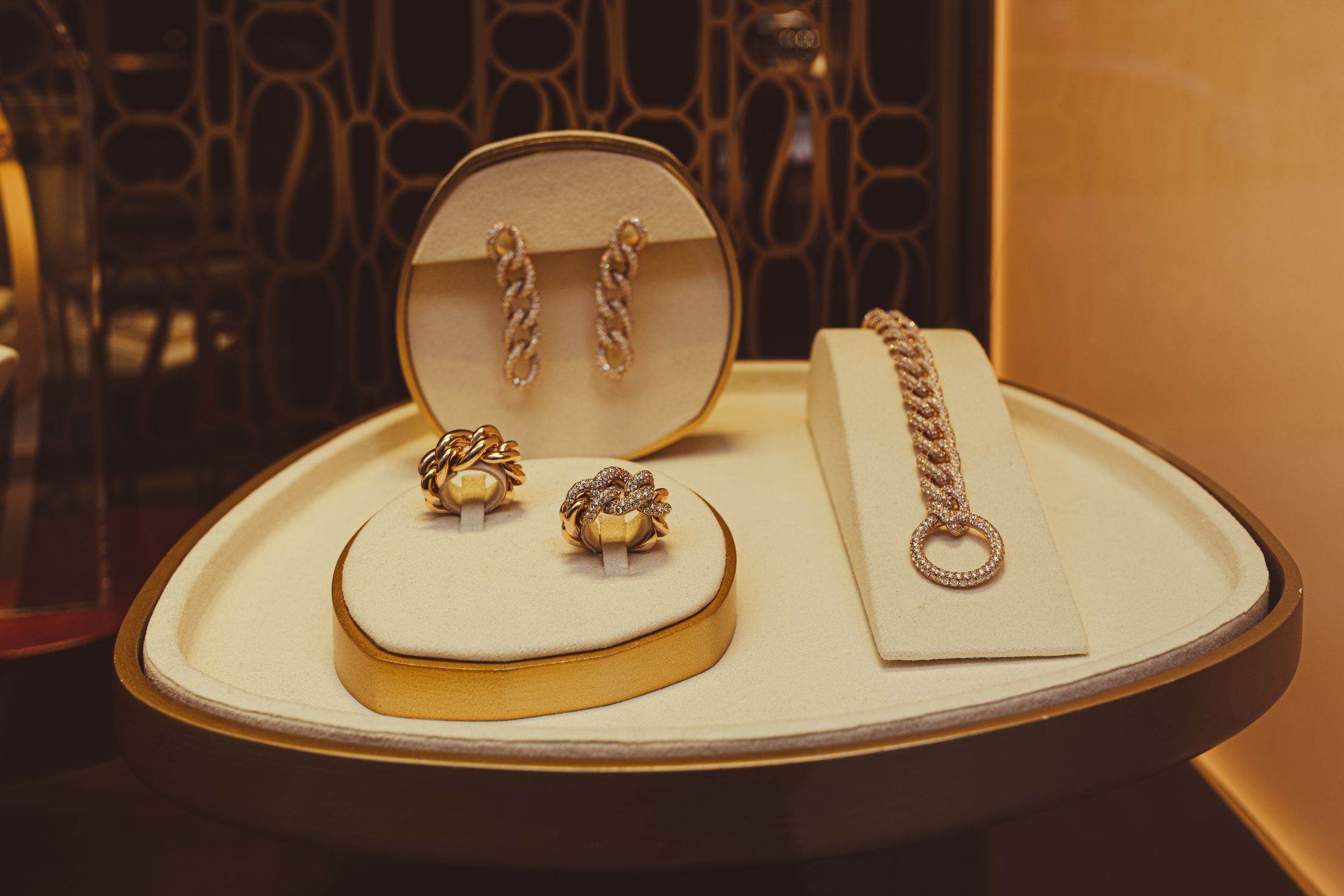 Gold earrings and a gold chain displayed on a cream jewellery tray