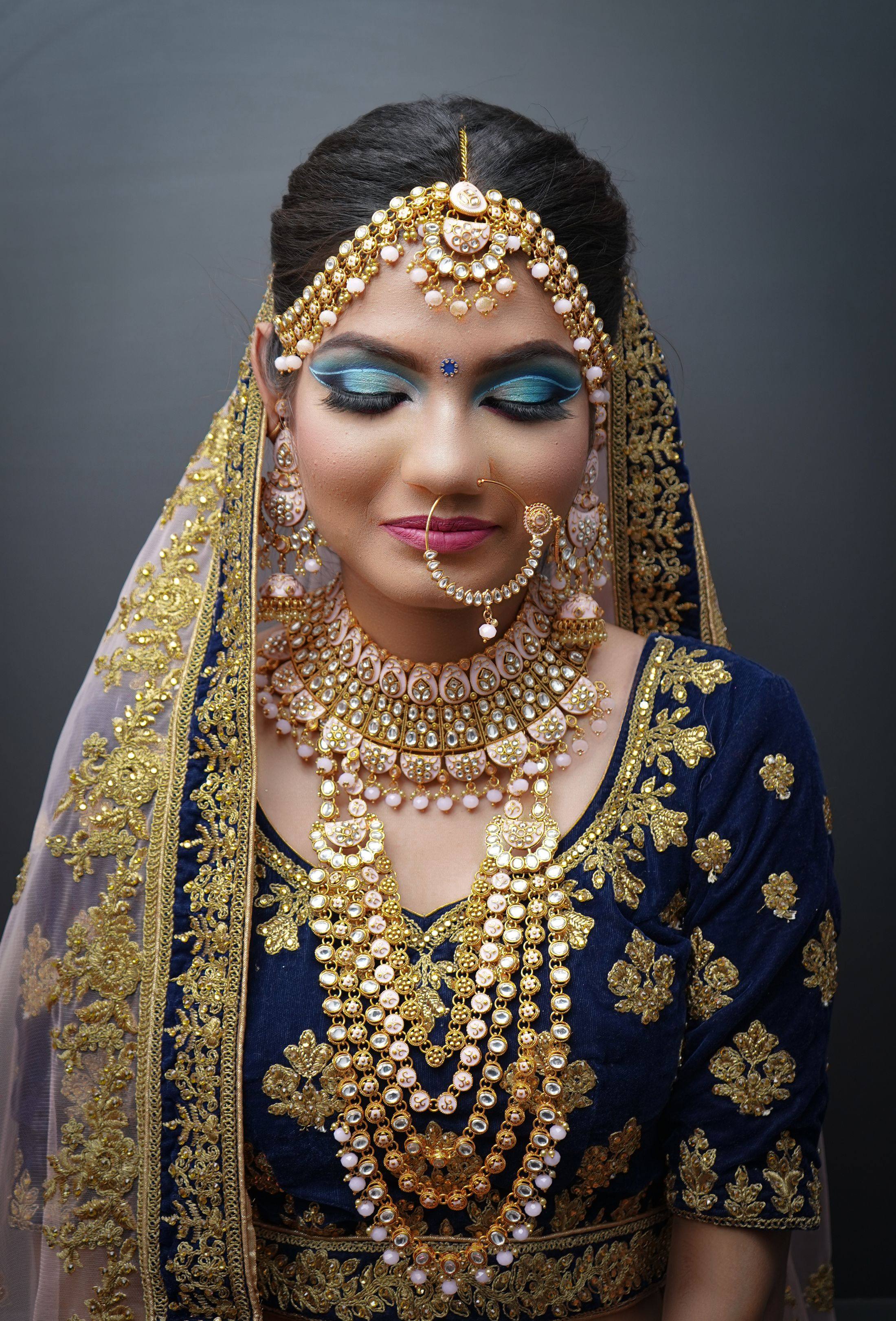 A bride in a royal-blue velvet blouse wearing a layered gold necklace, earrings and maang tikka