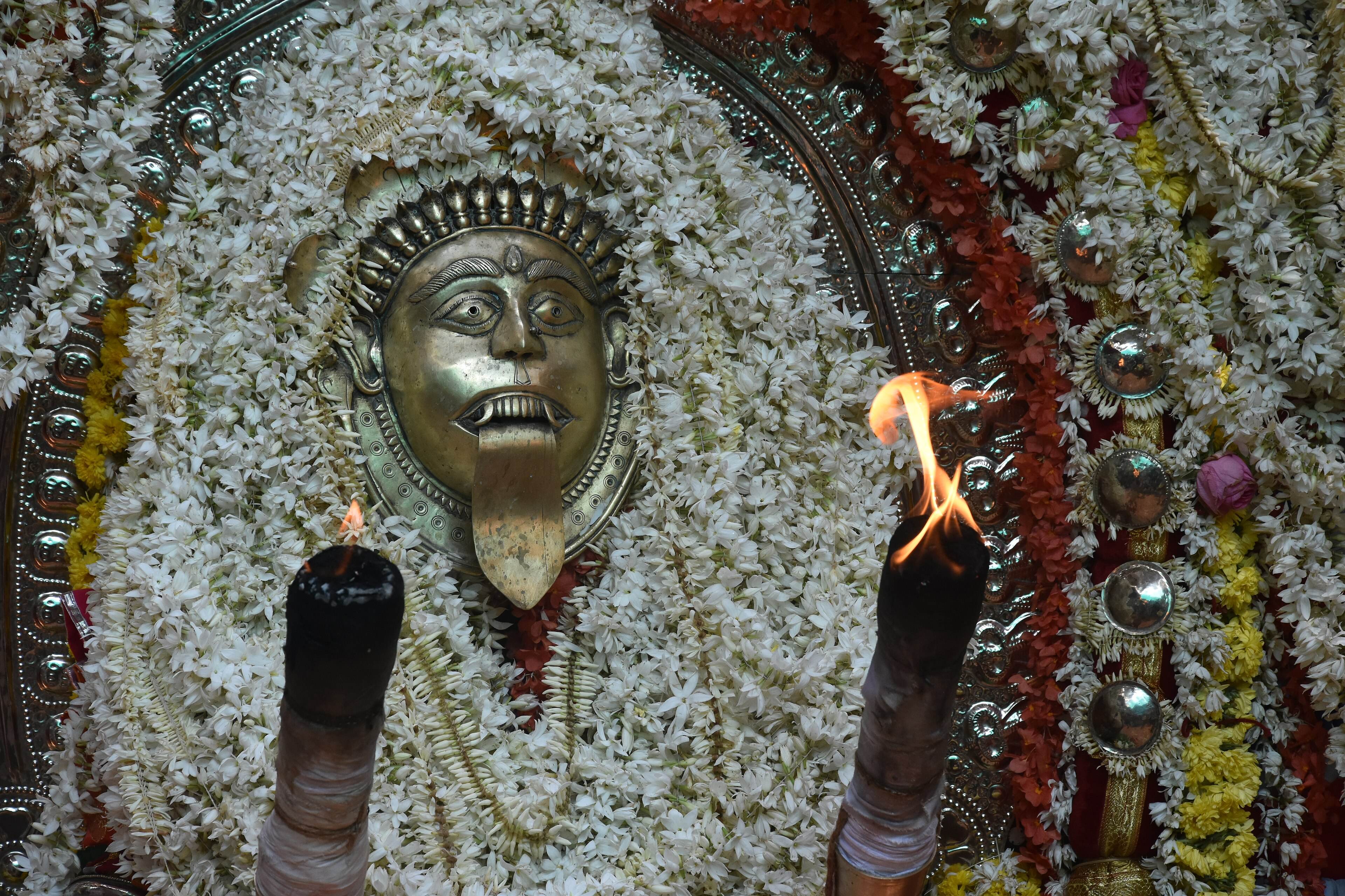 A metal Jumadi mask surrounded by flowers and flames during a Bhuta Kola ceremony